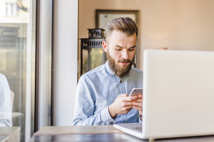 young-man-using-cellphone-with-laptop-desk-1